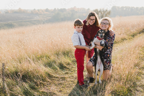 Samesex caucasian lesbian family with a child and a dog walking outdoors on the background of beautiful nature. Mothers having fun with their son.