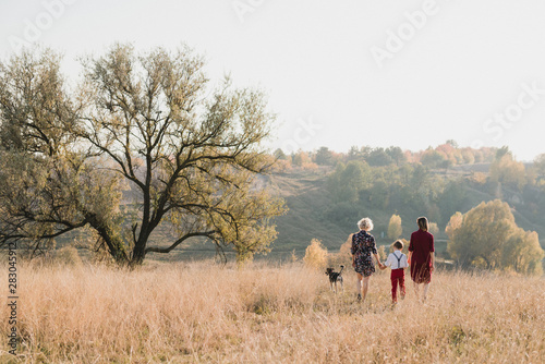 Samesex caucasian lesbian family with a child and a dog walking outdoors on the background of beautiful nature. Mothers having fun with their son.