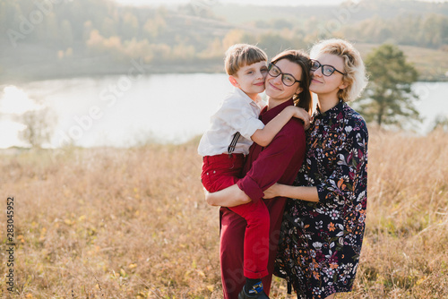 Samesex caucasian lesbian family with a child and a dog walking outdoors on the background of beautiful nature. Mothers having fun with their son.