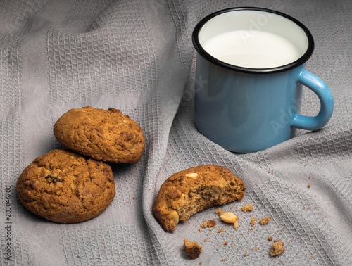Mug of milk and oat cookies with crumbs on grey towel