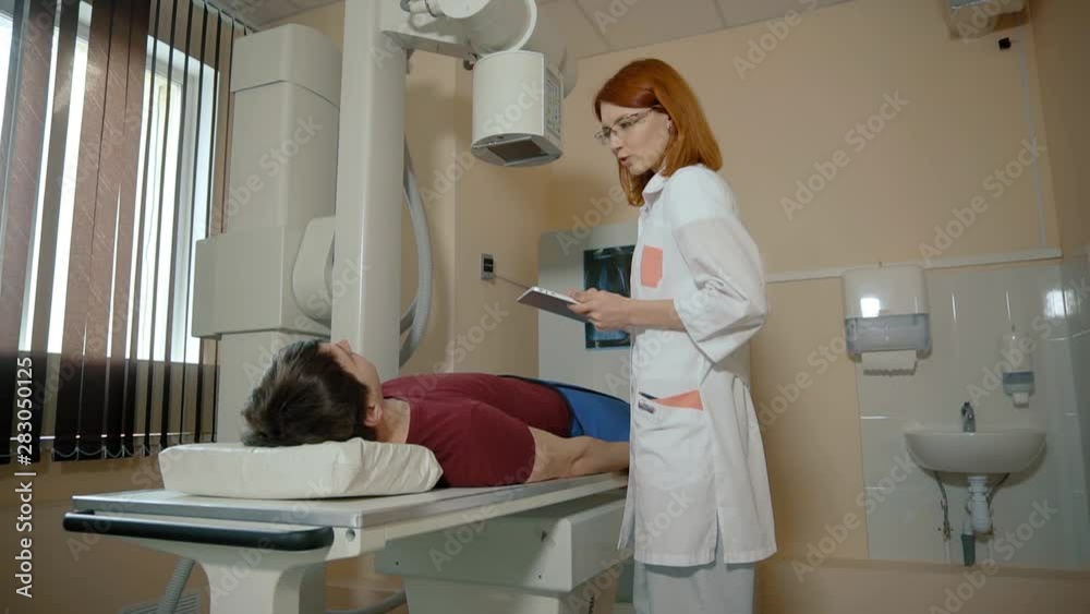 Patient man lies on the bed, x-ray examination. Female doctor prepares an x-ray machine for work Patient man lies on the bed, x-ray examination. Female doctor prepares an x-ray machine for work