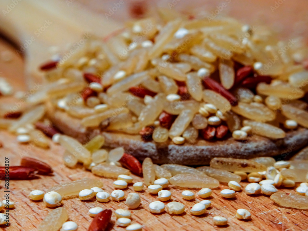 Mix red rice, complete rice, quinoa uncooked on wooden spoon and wooden surface Mix red rice, complete rice, quinoa uncooked on wooden spoon and wooden surface