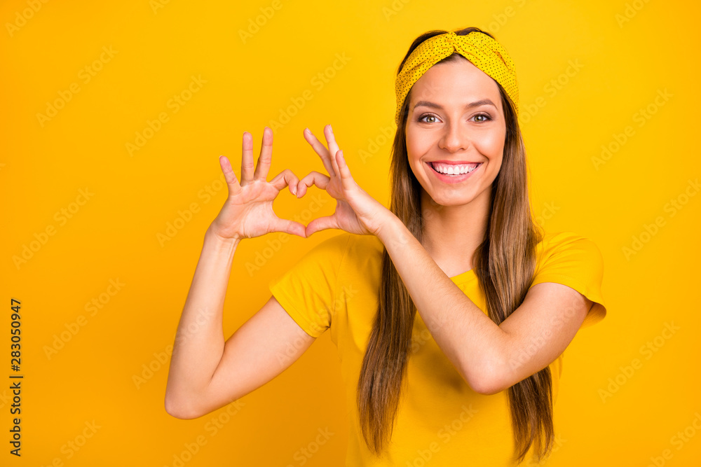Portrait of lovely millennial making heart form with her hands smiling wearing t-shirt isolated over yellow background Portrait of lovely millennial making heart form with her hands smiling wearing t-shirt isolated over yellow background