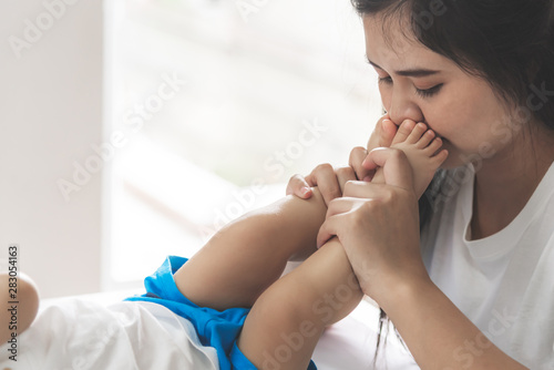 Asian mother kissed her baby's feet, With love and tie, to Mother's Day and relationship concept