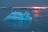 Arctic nature landscape with icebergs in Greenland icefjord with midnight sun sunset / sunrise in the horizon.  Early morning summer alpenglow during midnight season. Ilulissat, West Greenland.