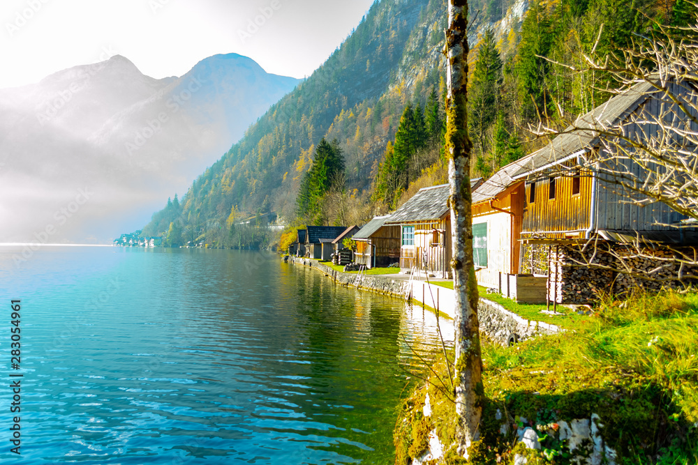 Fototapeta premium Mountain Lake. Surrounded by rocky mountains covered with pine trees. Close to the water are wooden houses. fog above the water. Daytime