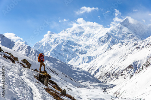 Strong girl with backpack Osprey stands on the edge of the mountain overlooking the snow-capped peaks of the Himalayas on Annapurna Circuit Trek in Nepal.