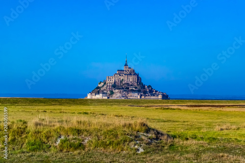 Stunningly beautiful medieval castle of Mont Saint Michel. Abbey  located on the island  enclosed by fortifications. It is washed by the sea from all sides. Beautiful blue sky and fluffy white clouds