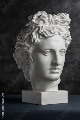 Gypsum copy of ancient statue Apollo head on dark textured background. Plaster sculpture man face.