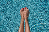 Beautiful woman legs sunbathing near swimming pool. Perfect Red Pedicure.