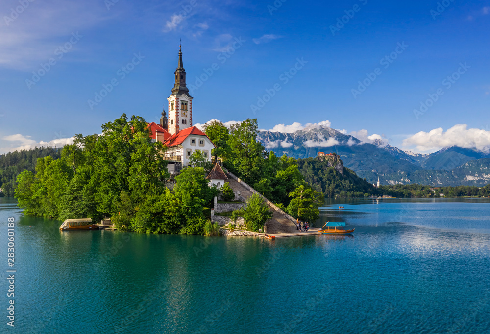 Bled, Slovenia - Lake Bled (Blejsko Jezero) with the Pilgrimage Church of the Assumption of Maria, pletna boats, Bled Castle and Julian Alps on a sunny summer day with blue sky