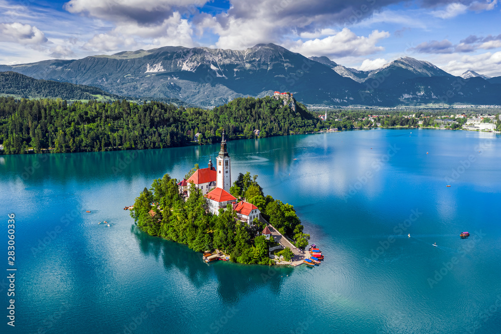 Bled, Slovenia - Aerial view of Lake Bled (Blejsko Jezero) with the Pilgrimage Church of the Assumption of Maria, pletna boats, Bled Castle and Julian Alps on a sunny summer day