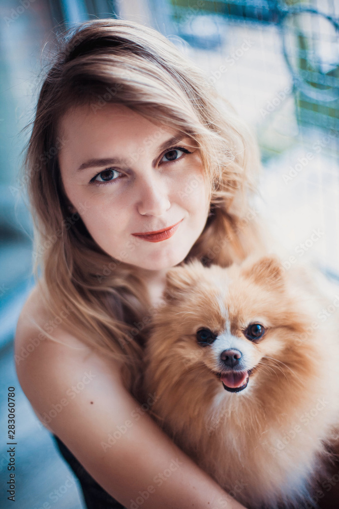 Close up portrait of smiling young attractive woman embracing Pomeranian spitz.