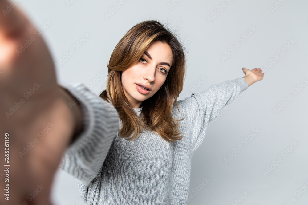 Attractive woman dressed casually having delightful look smiling broadly. Beautiful woman having cheerful expression while posing against gray background, stretching arm to camera.