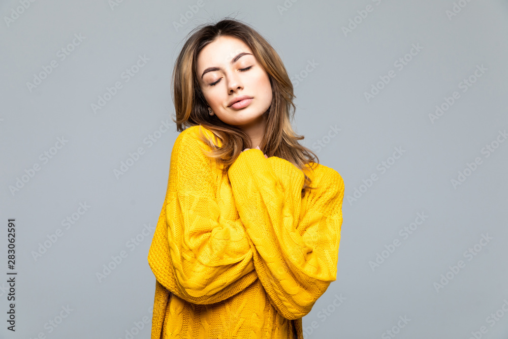 Young beautiful woman in yellow casual sweater standing with arms crossed isolated on gray background