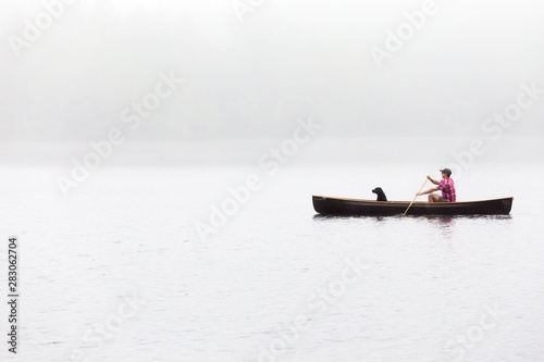Wide shot of a male with black dog riding boat on a lake