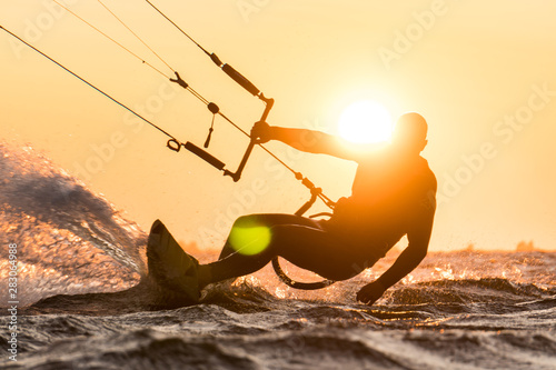 Silhouette of kitesurfer riding in beautiful sunset conditions with sun next to the riders head photo