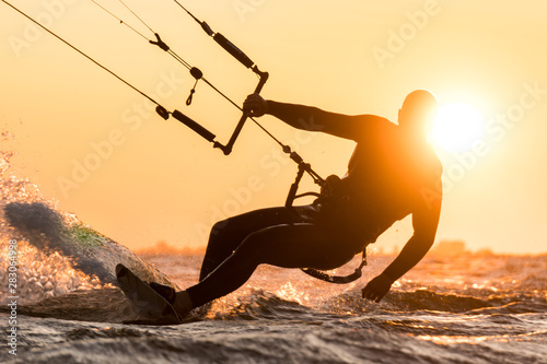 Fototapeta Naklejka Na Ścianę i Meble -  Silhouette of kitesurfer riding in beautiful sunset conditions with sun behind and lens flare