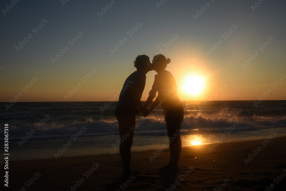 Romantic couple kissing on the beach with a beautiful sunset in background. Happy couple on summer vacation hugging and kissing at sunset