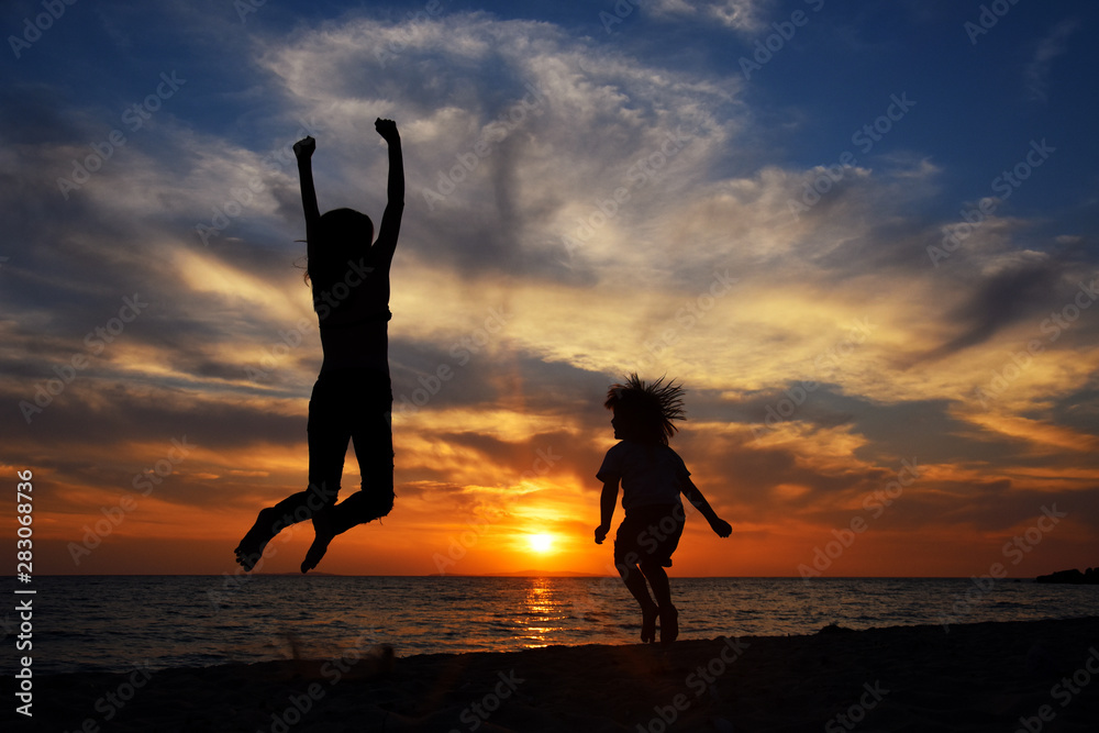 Happy young family have fun on beach and jump at sunset. Silhouette of mom and son jump at sunset