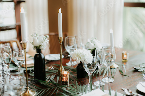 modern and bohemian table decorations at wedding reception, table setting with candle sticks, palm leafs, and flowers