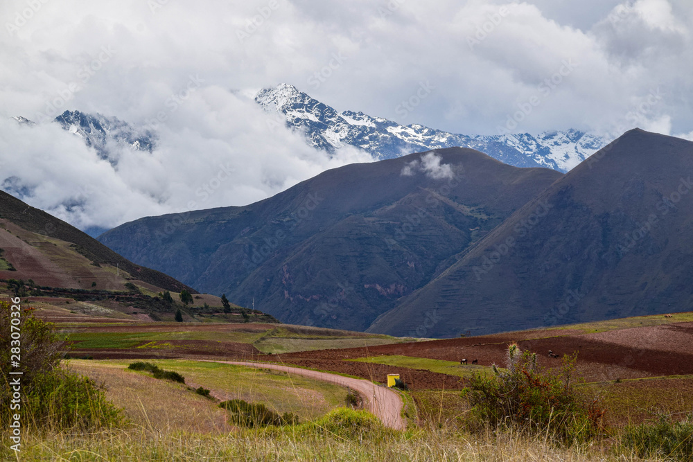 Empty road going through the farm lands in Sacred Valley in Peru with the mountains in the background