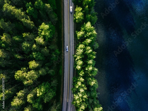 Aerial landscape view of road between green pine forest and blue lake in Finland