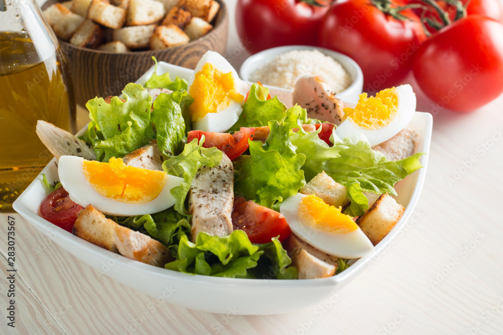 Fresh Caesar salad with delicious chicken breast, ruccola, spinach, cabbage, arugula, egg, parmesan and cherry tomato on wooden background. Oil, salt and pepper. Healthy and diet food concept. Fresh Caesar salad with delicious chicken breast, ruccola, spinach, cabbage, arugula, egg, parmesan and cherry tomato on wooden background. Oil, salt and pepper. Healthy and diet food concept.