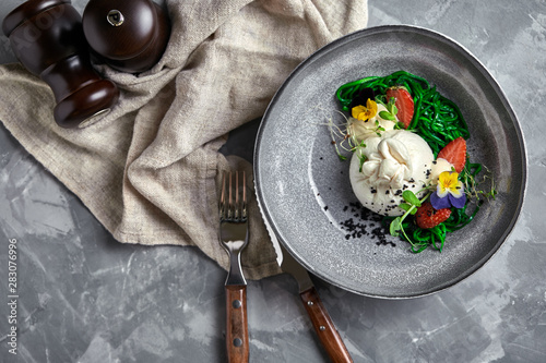 Fototapeta Naklejka Na Ścianę i Meble -  Burrata salad with strawberries and seaweed, on a gray background. Salad with buratta cheese on a gray plate and concrete marble background.