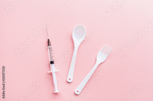 Medical syringe, plastic spoon and fork on pink background, health and vaccination concept. Flat lay, mockup, overhead, top view and copy space.
