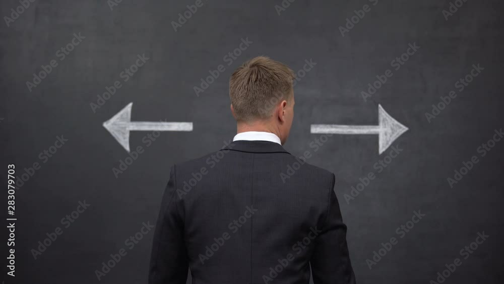Businessman standing between arrows showing different directions, back view Businessman standing between arrows showing different directions, back view