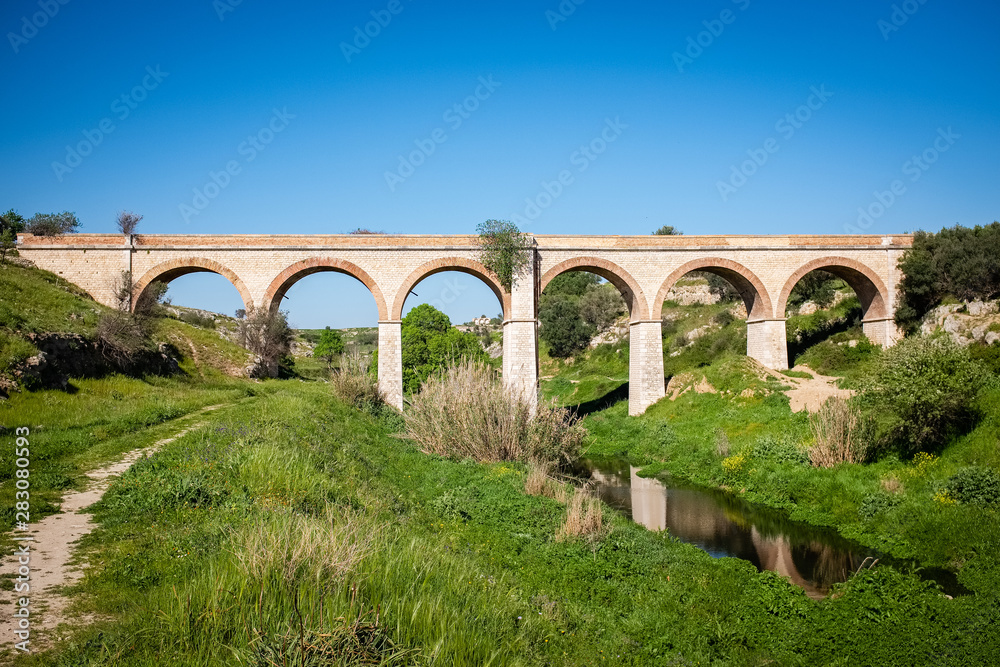 Beautiful old stone bridge of abandoned railway crossing a small river. Puglia region, Italy