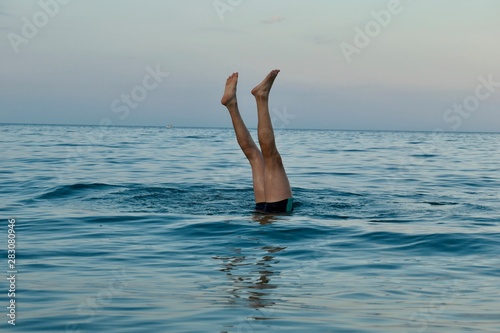 A man is doing a handstand in the sea and only his feet can be seen. Other people are swimming nearby