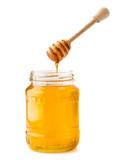 Honey flows down from a wooden stick into a glass jar on a white, isolated.