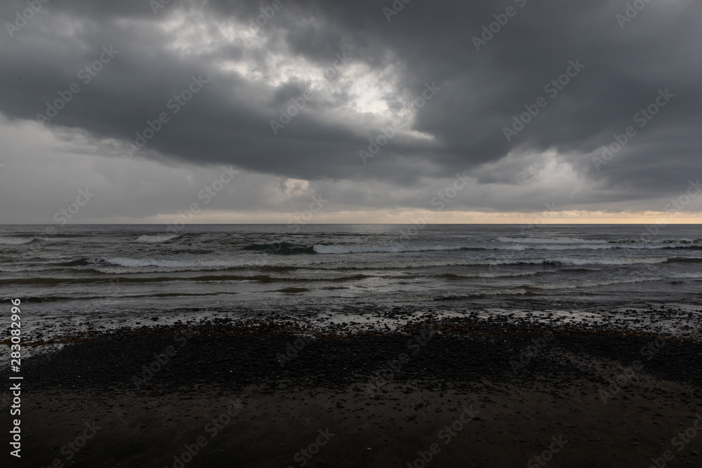 Black sand beach with green vegetation in a stormy day in Bali, Indonesia