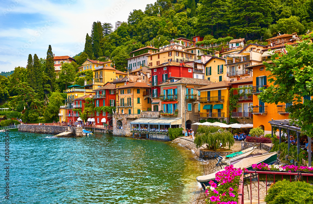 Varenna, Italy. Picturesque town at lake Como. Colourful motley Mediterranean houses on knoll by coastline among green trees. Popular health resort and touristic destination location. Summer day.