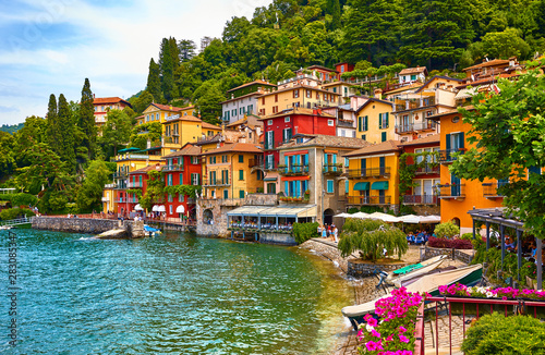 Fototapeta Naklejka Na Ścianę i Meble -  Varenna, Italy. Picturesque town at lake Como. Colourful motley Mediterranean houses on knoll by coastline among green trees. Popular health resort and touristic destination location. Summer day.
