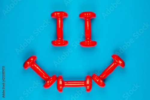 A smiley face made from red dumbbells on blue background, shot from above.