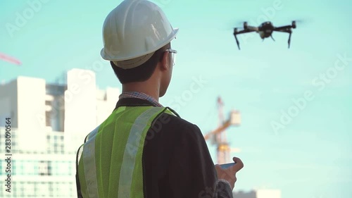 Man architect controlling flying drone for aerial view. Portrait of a successful engineer, builder using smartphone to control the quadcopter. Modern technologies in construction, and architecture