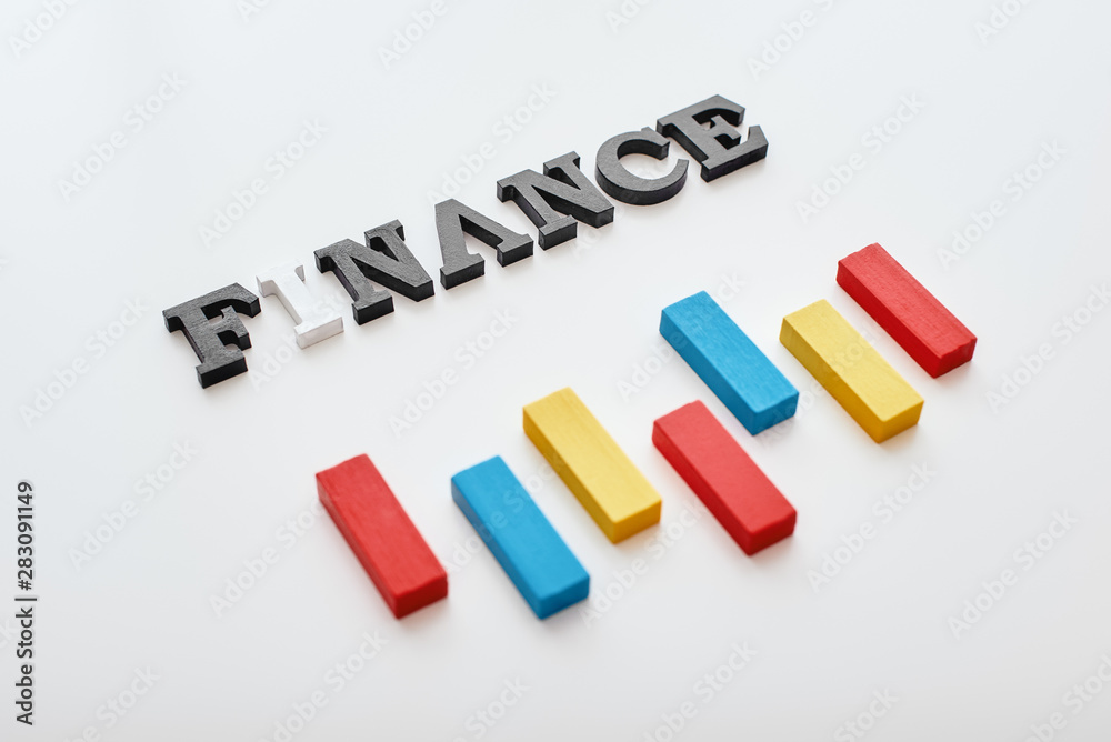 Finance word created with cubes alphabet letters near multi-colored wooden blocks lying diagonally Finance word created with cubes alphabet letters near multi-colored wooden blocks lying diagonally