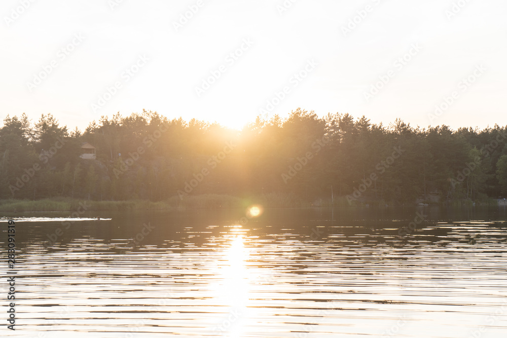 Fototapeta premium View of the water in the ripples in the quarry, on the silhouette of the forest on the opposite bank. Summer orange sunset. 