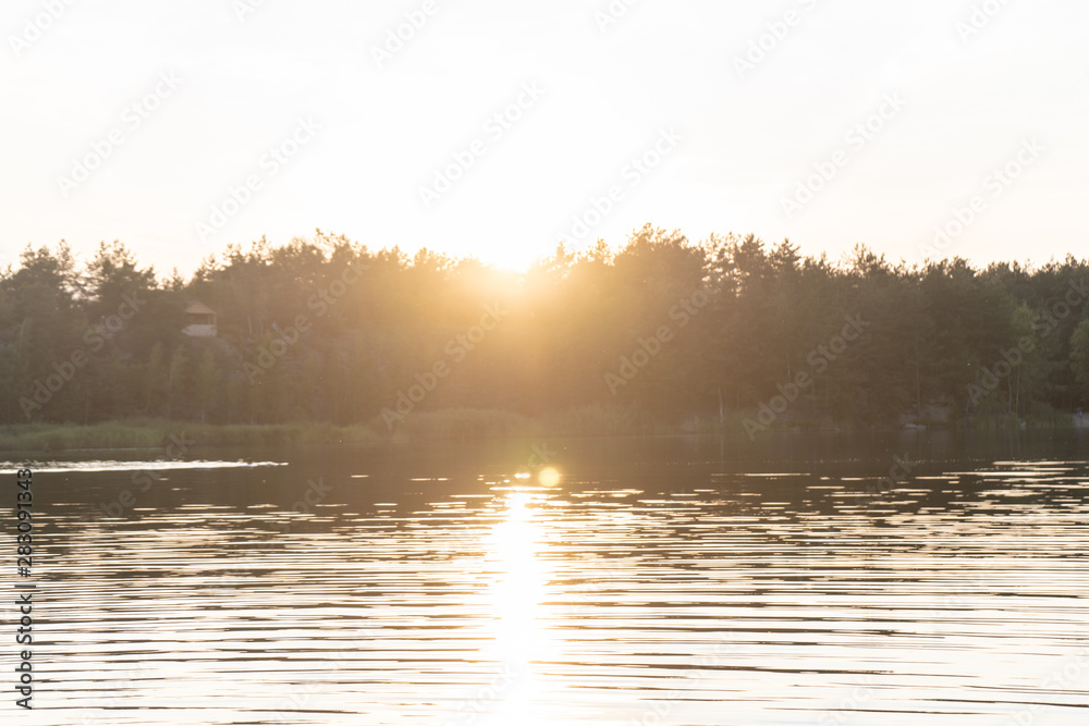 Picturesque landscape. View of the water in the ripples in the quarry, on the silhouette of the forest on the opposite bank. Summer orange sunset. 