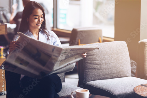 What's new? Asian business woman reading newspaper and drinking coffee in the morning in cafe. Copy space on the right side