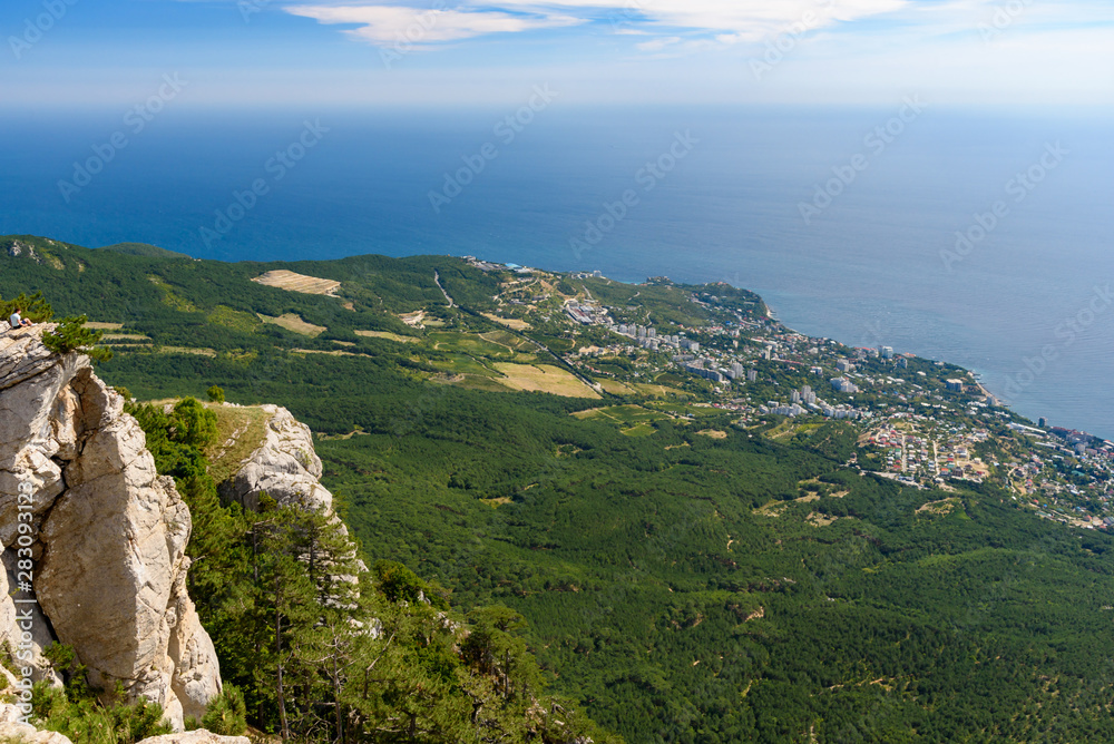 view of the resort city of Yalta from the top of Mount Ai-Petri, on a bright sunny day with clouds in the sky.