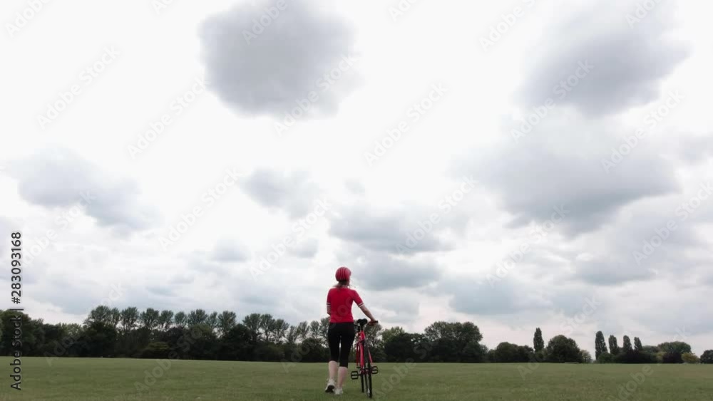 Caucasian female cyclist in red top walking with her bike in a park Caucasian female cyclist in red top walking with her bike in a park