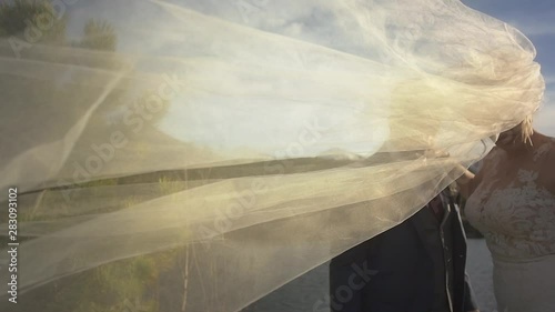 A bride's veil flows across the frame at an outdoor wedding in the evening