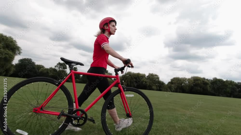 Caucasian female cyclist in red top walking with her bike in a park Caucasian female cyclist in red top walking with her bike in a park