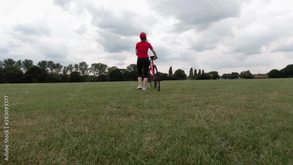 Caucasian female cyclist in red top walking with her bike in a park Caucasian female cyclist in red top walking with her bike in a park