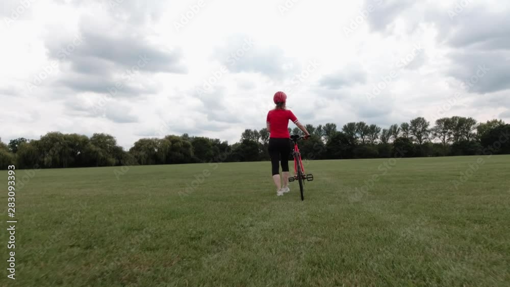 Caucasian female cyclist in red top walking with her bike in a park Caucasian female cyclist in red top walking with her bike in a park
