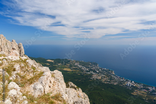 view of the resort city of Yalta from the top of Mount Ai-Petri, on a bright sunny day with clouds in the sky.